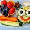 Pomysł na śniadanie dla dziecka do szkoły -zdjęcie ilustracyjne wpisu na bloga przedstawiające kanapkę przyponijącą buźkę, pokrojone warzywa i owoce w pojemniki