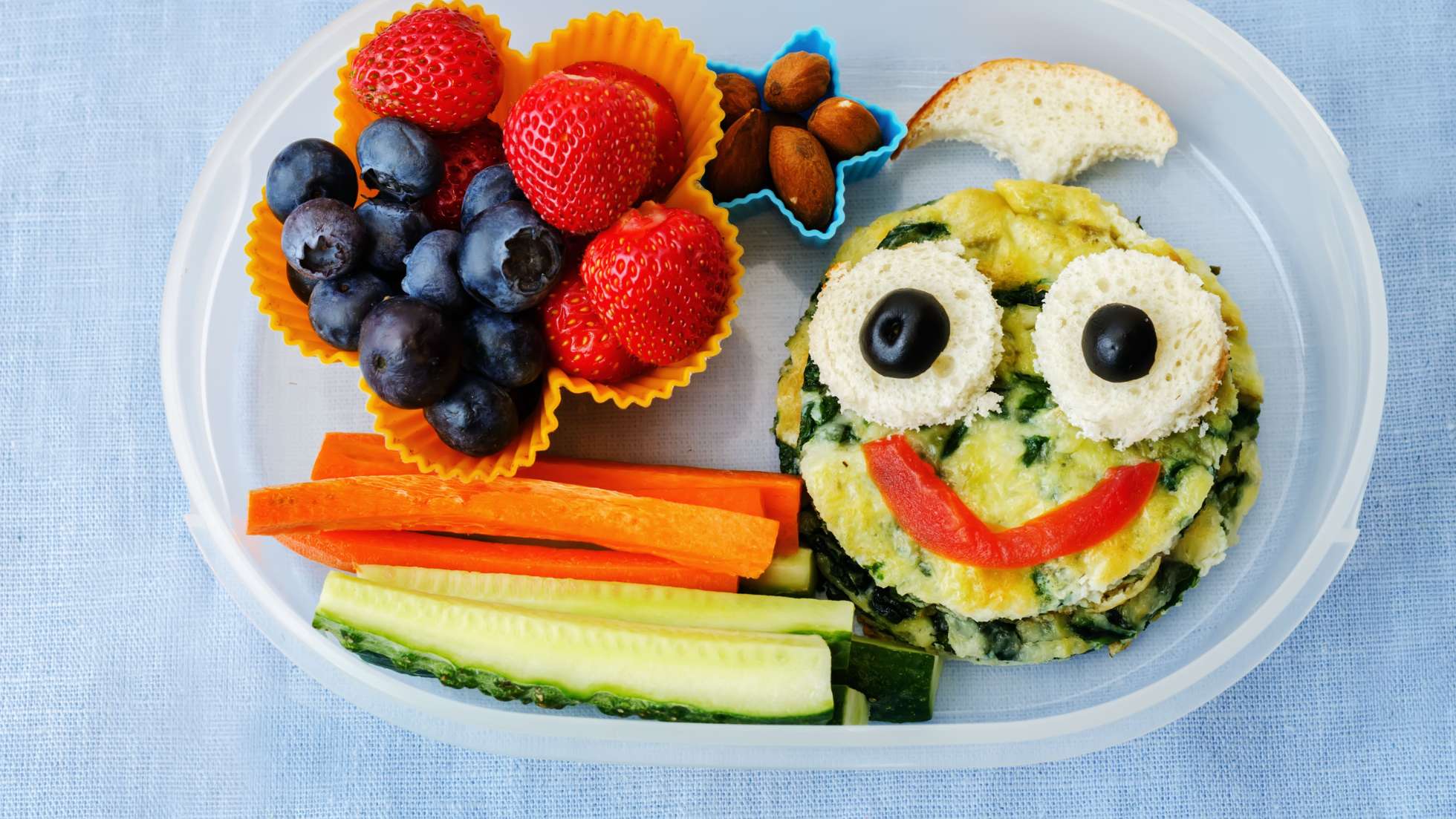 Pomysł na śniadanie dla dziecka do szkoły -zdjęcie ilustracyjne wpisu na bloga przedstawiające kanapkę przyponijącą buźkę, pokrojone warzywa i owoce w pojemniki