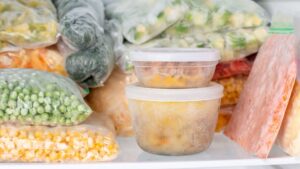 Zdjęcie ilustracyjne wpisu na bloga pt "Pojemniki do przechowywania żywności – jak dobrać do rodzaju żywności." Zdjęcie przedstawia zamrożone warzywa w zamrażarce. Warzywa w pojemniku plastikowym i woreczkach.