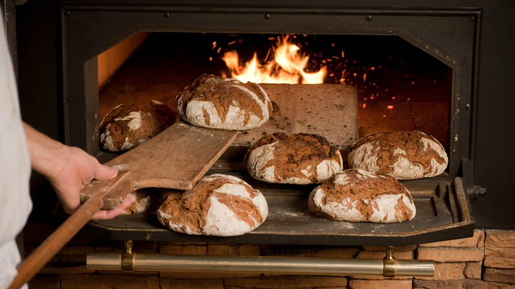 Zdjęcie przedstawia bochny chleba wyjmowanie z pieca piekarniczego opalanego ogniem