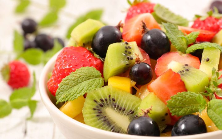 3 przepisy na sałatkę owocową – smakowity posiłek w czasie upałów - zdjęcie ilustracyjne wpisu na bloga. Zdjęcie przedstawia miskę z pokrojonymi owocami: kiwi, truskawka, winogrona